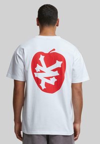 Hvid bomulds-t-shirt med et stort rødt æblegrafik og et hvidt knoglemønster på ryggen. Korte ærmer og en afslappet pasform.