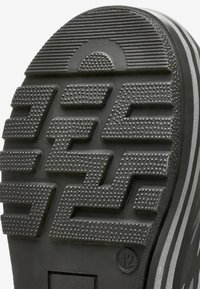 Semelle de chaussure en caoutchouc noir avec un motif de bande de roulement en zigzag, présentant de petits points surélevés et des rainures horizontales, marquée de la taille 12.