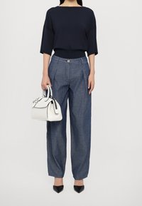 Marinblå översize topp, lösa blå chambraybyxor med veck, svarta spetsiga klackskor och en vit handväska med svarta detaljer.