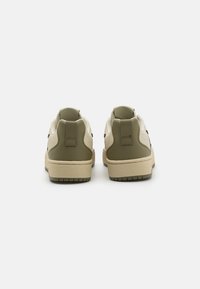 Sleek sneakers with a beige and olive green upper, smooth leather heel, and textured rubber sole, featuring subtle perforations and stitching detail.