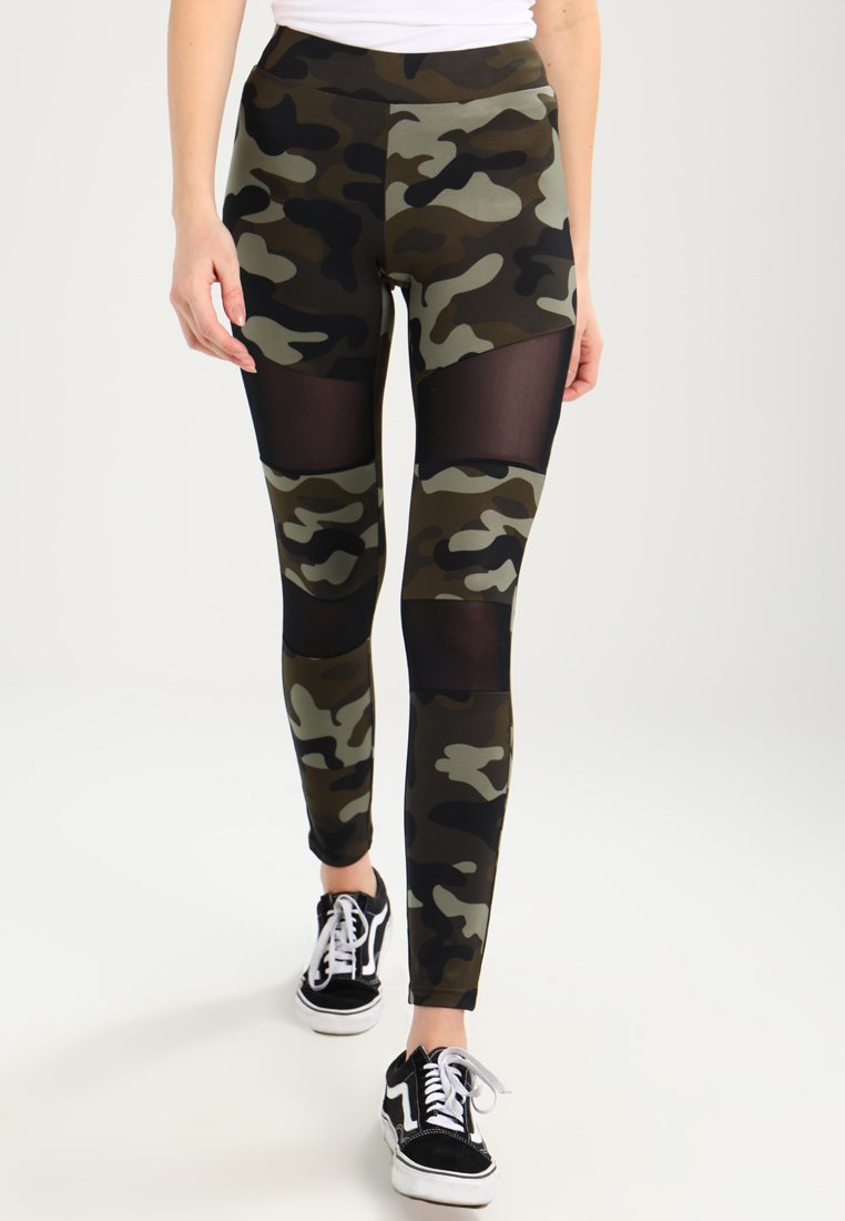 Kamouflageleggings i grönt och svart med nätpaneler, hög midja och åtsittande design. Kombinerat med svarta sneakers med vita snören.