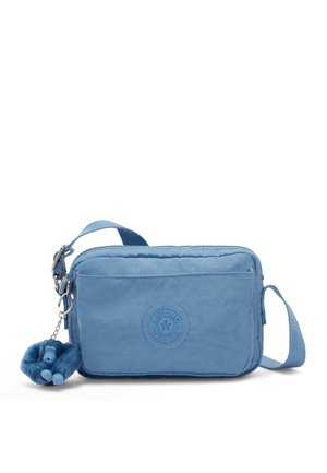 Bolso pequeño azul cruzado con bolsillo delantero y logo redondo, que cuenta con un llavero peludo de mono azul adjunto al lateral.