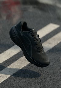 Μαύρο αθλητικό παπούτσι με υφασμάτινο επάνω μέρος, στρογγυλεμένη μύτη και λαστιχένια σόλα. Διαθέτει χοντρές κορδόνια και λογότυπο swoosh στο πλάι.