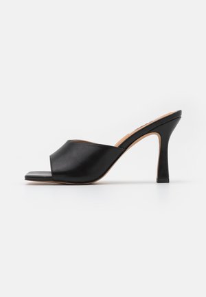 Mules de tacón abiertas en punta de cuero negro que cuentan con un diseño curvado, un acabado ligeramente brillante y un tacón delgado y resistente.