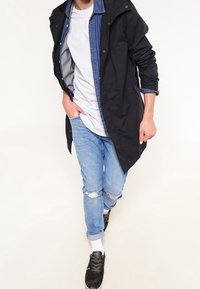 Giacca leggera nera, camicia di denim con bottoni, t-shirt bianca, jeans strappati azzurri chiari e sneakers nere in camo. Outfit casual con texture sovrapposte.