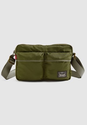 Oliwkowa torba crossbody z dwiema przednimi kieszeniami, regulowanym paskiem, czerwoną metką Levi's oraz naszywką z logo Levi Strauss & Co. z przodu.