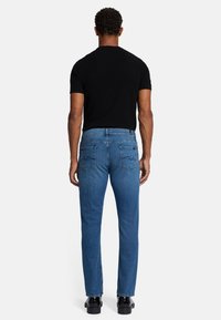 Jeans in denim blu con taglio dritto, cinque tasche e cuciture visibili. Indossati con una maglietta nera a maniche corte e scarpe nere.