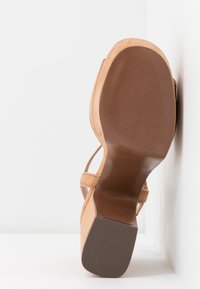 Tan semišové sandály na vysokém podpatku s texturovanou hnědou gumovou podrážkou, kterými se vyznačují tenké popruhy a tvarovaný podpatek.