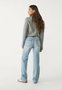 Pullover grigio lavorato a maglia e jeans svasati azzurri chiari. I jeans presentano tasche posteriori e una finitura invecchiata. Il modello è di spalle rispetto alla macchina fotografica.