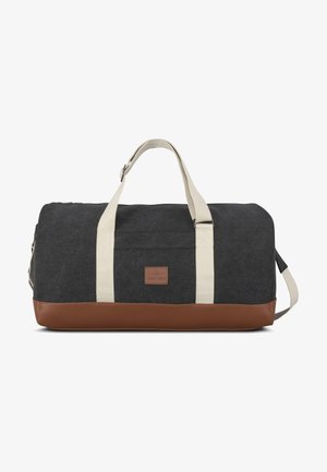 Sac de sport en tissu gris foncé avec des sangles crème et un fond en cuir marron. Présente un patch logo et une fermeture éclair. Forme rectangulaire compacte.