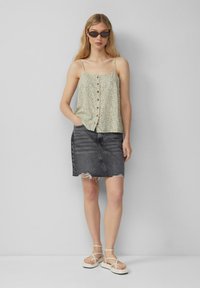 Lichtgroene cami met bloemenpatroon en knoopsluiting, gecombineerd met een versleten zwart denim minirok. Model draagt sandaaltjes met bandjes.