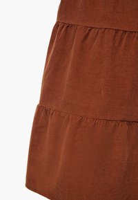 Tissu en velours côtelé marron avec des volants froncés formant une jupe ou un détail de robe sur un fond uni.