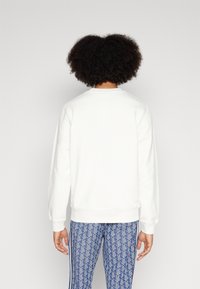 Vit sweatshirt med långa ärmar, rund hals och ribbade ärmar. Matchad med blå mönstrade leggings med vertikala ränder.