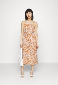 Vestido castanho com padrão e desenhos florais brancos e abstratos, alças finas, de comprimento médio, combinado com uma bolsa branca e sandálias.