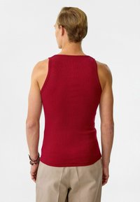 Rode geribbelde tanktop met een aansluitend ontwerp, voorzien van een ronde halslijn en brede schouderbanden. De stof lijkt glad en rekbaar.