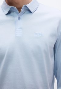 Ανοιχτό μπλε μακρυμάνικο πόλο από απαλό βαμβάκι. Διαθέτει κλασικό γιακά, δύο κουμπιά και κεντητό λογότυπο "BOSS" στο ίδιο χρώμα.