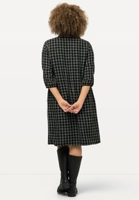 Zwart en grijs geruit langwerpig jurkje met een relaxed fit, met een middellange zoom en gedragen met hoge zwarte laarzen tot de knie.