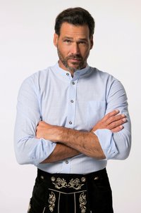 Camisa de botones azul claro con cuello mao, mangas cortas y bolsillo en el pecho; combinada con pantalones tradicionales negros con bordados plateados ornamentales.