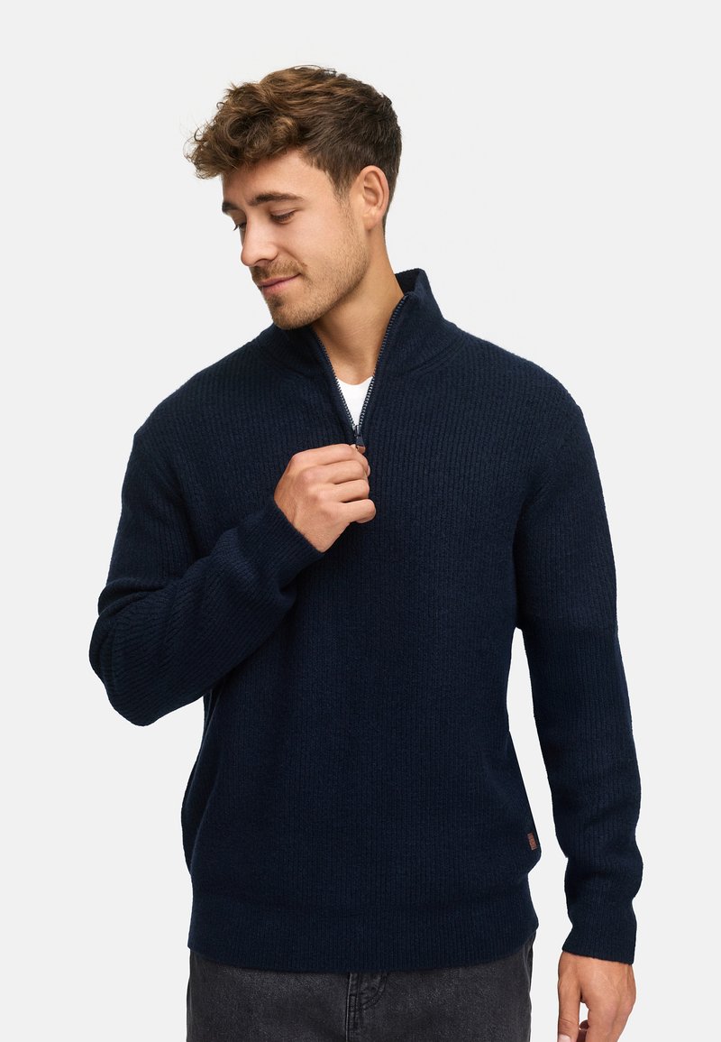 Pull en tricot côtelé marine avec col montant et fermeture à demi-zip ; fabriqué dans un matériau doux, avec des manches longues et une coupe décontractée.