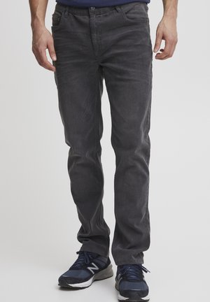 Jean en denim gris à coupe slim, cinq poches, décoloration subtile et fermeture éclair. Porté avec des chaussures de sport bleu marine pour un look décontracté.