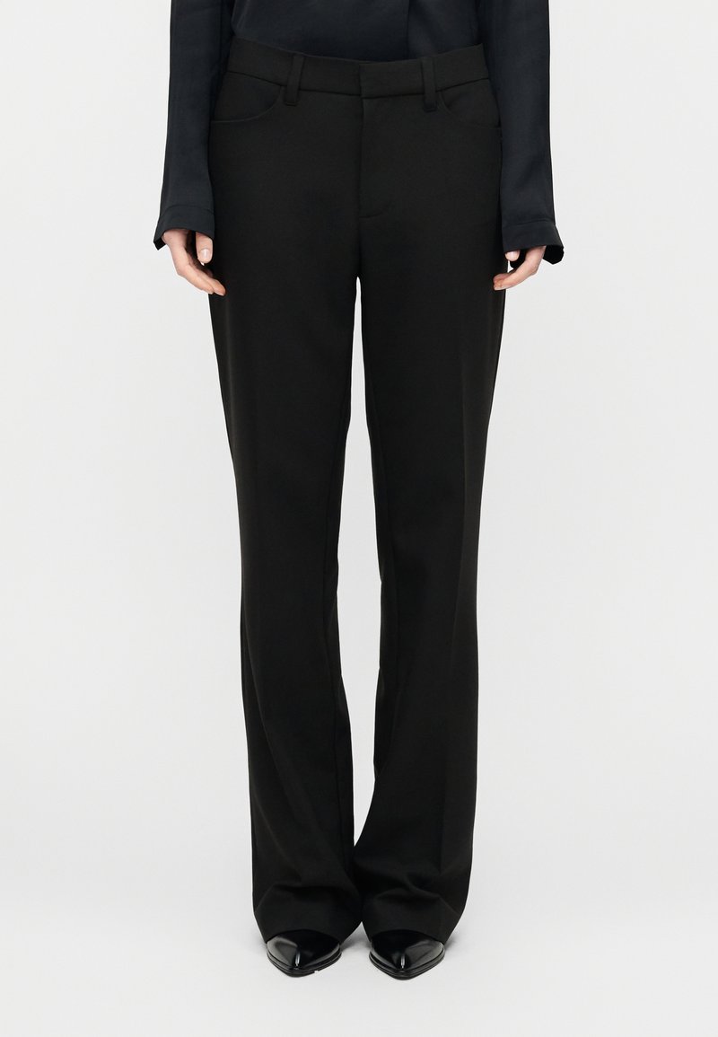 Μαύρο παντελόνι σε στενή γραμμή, κατασκευασμένο  από λείο ύφασμα, με ευθύ κόψιμο, θηλιές για ζώνη και μπροστινές τσέπες. Συνδυάζεται με μυτερά μαύρα παπούτσια.