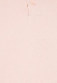 Lyserød polo t-shirt med ribbet tekstur, tre-knap åbning og korte ærmer. Blødt stof uden synlige mønstre eller detaljer.