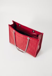 Sac fourre-tout en simili cuir rouge avec un motif texturé, poignées en chaîne argentées et une ouverture sur le dessus, comportant une poche zippée à l'intérieur.