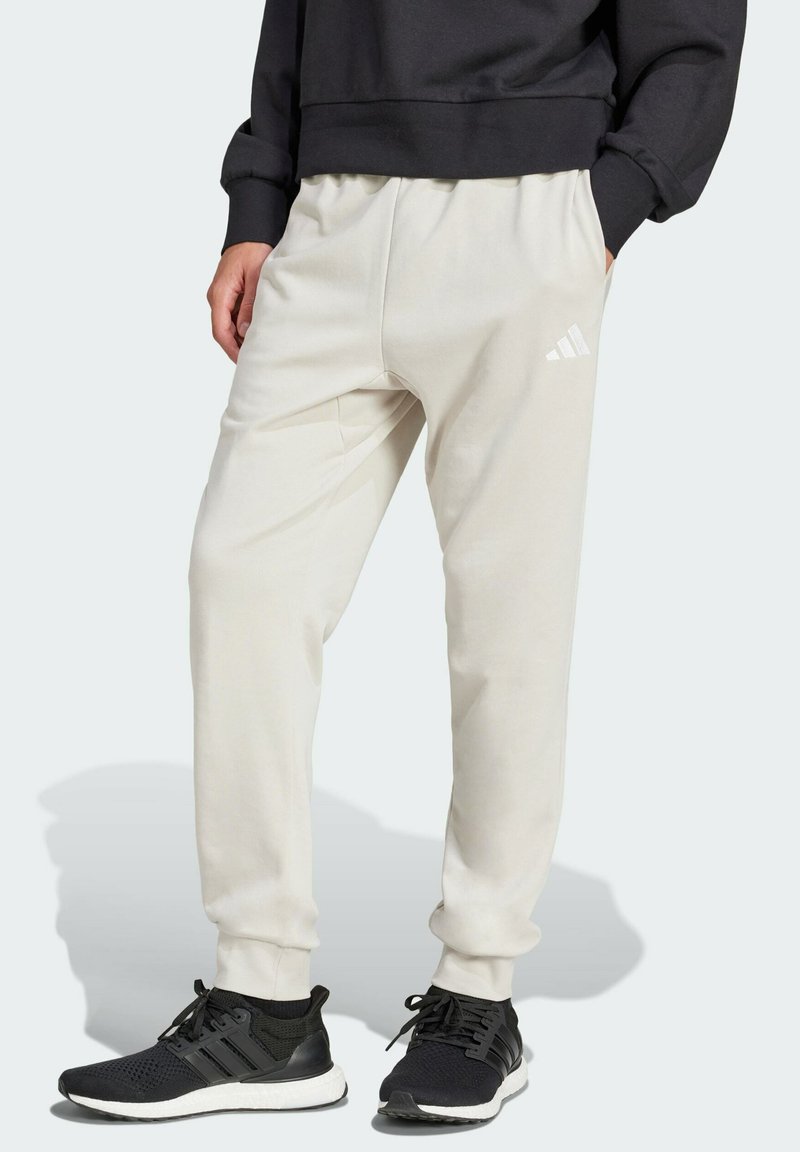 Ljusbeige sweatpants med en avslappnad passform, med ett elastiskt midjeband och sidofickor. Accentuerade av en vit Adidas-logga pålåret.