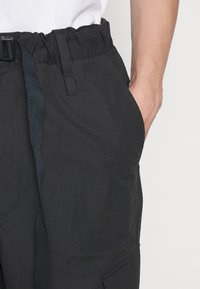 Zwarte broek met elastische tailleband, verstelbare trekkoord, gestructureerde stof en zijzakken voor een functioneel ontwerp.