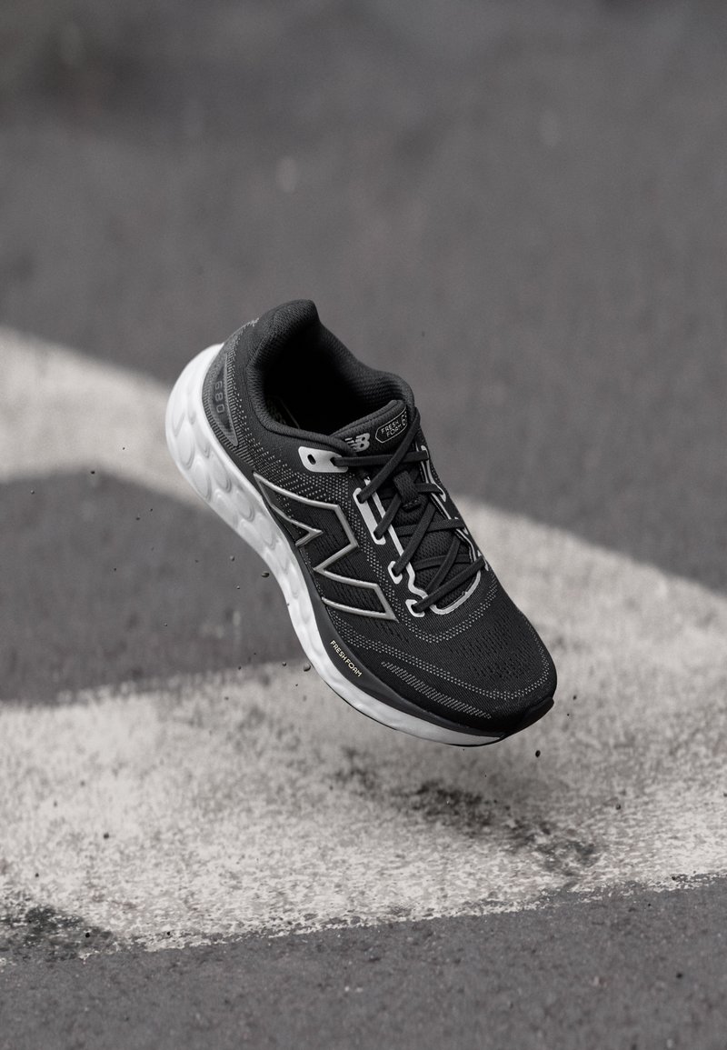 Chaussure de sport noire avec un dessus texturé, un amorti réactif et des accents blancs. Présente un design à lacets et une coque renforcée à l'avant.