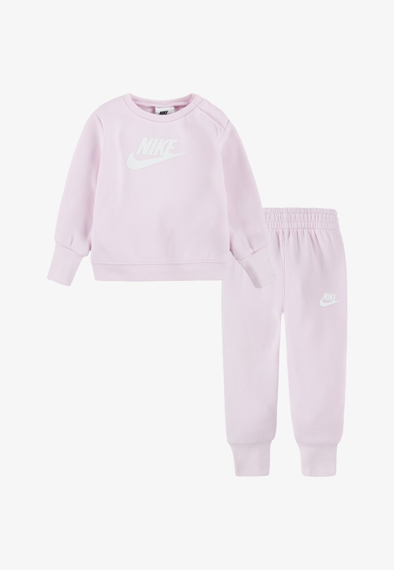 Rožinė sportinė palaidinė ir suderintos jogger tipo kelnės, pagamintos iš minkštos medžiagos, su baltu Nike logotipu priekyje ir ant kojos. Kelnėse - elastinga juosta.