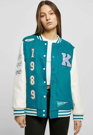 Veste varsity teal et blanche avec un devant à boutons, des poignets côtelés et des patchs brodés, mettant en avant l'année "1989" et des détails "NYC".