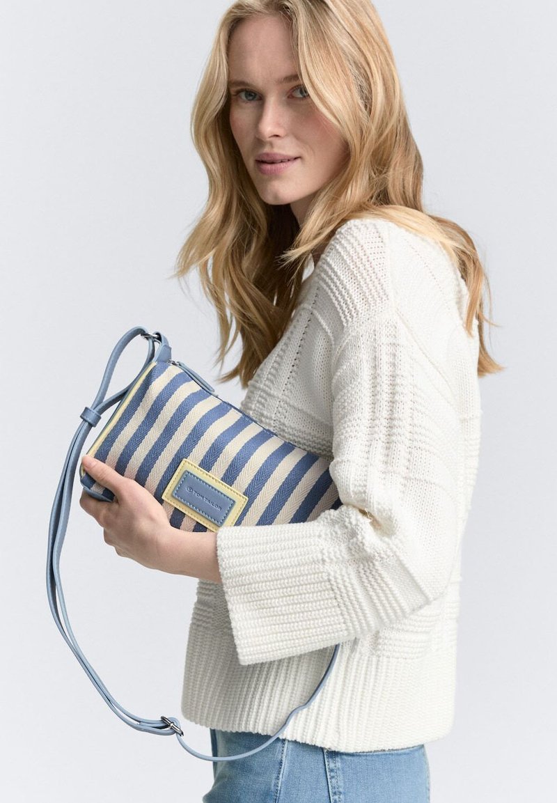 Sac à épaule en toile rayée avec des rayures bleues et blanches, une bandoulière bleu clair et un accent jaune. Surface texturée avec un patch logo rectangulaire.
