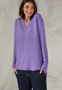 Pull-over lavande à col en V avec un design tricoté à nervures texturé et des épaules tombantes, associé à un jean bleu foncé et ample.