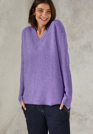 Pull-over lavande à col en V avec un design tricoté à nervures texturé et des épaules tombantes, associé à un jean bleu foncé et ample.