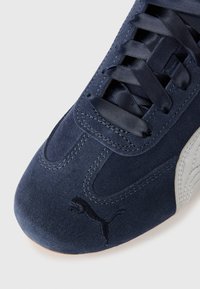 Niebieskie zamszowe sneakersy z zaokrąglonym noskiem, ciemnoniebieskimi sznurowadłami i srebrnym akcentem logo. Gładka tekstura i staranne detale szycia.