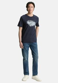 Mørkeblå bomulds t-shirt med grafisk print af en vintage bil,parret med lyseblå jeans og hvide sneakers. Enkel, afslappet design.