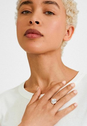 Hõberõngas roosimustriga, kantud käel. Modellil on lokkis blondid juuksed, seljas valge särk, käed loomuliku küünelakiga.