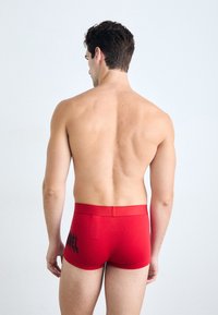 Rote Baumwoll-Boxershorts mit taillierter Passform, ausgestattet mit einem schwarzen Logo auf der linken Seite und einem glatten Bund. Der Stoff wirkt weich.