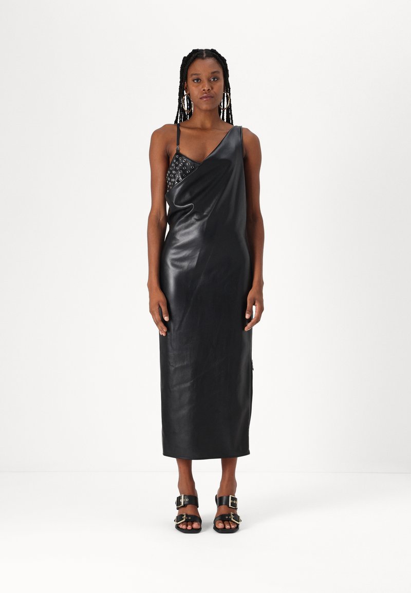 Svart skinnkjole med en skulderdesign, med en teksturert bodice. Modellen har på seg svarte sandaler med spenner, stående mot en hvit bakgrunn.