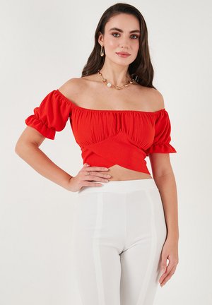 Red off-the-shoulder top with puff sleeves, textured fabric, and fitted design. Paired with white high-waisted pants featuring side stripes.