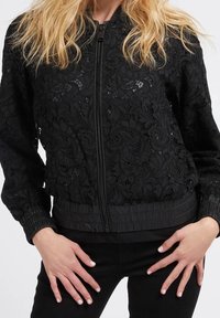 Black bomber jacket featuring a floral lace overlay, ribbed cuffs and hem, zip closure, and a textured, lightweight fabric.