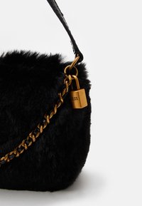 Czarna torebka na ramię z sztucznego futra z akcentami w postaci złotych łańcuszków, wyposażona w zamek i teksturowany pasek. Kompaktowy, zaokrąglony kształt.