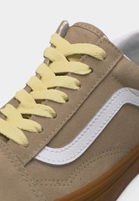 Artimos planas smėlio spalvos zomšinių sportbačių su geltonais raišteliais, baltos odos šonine juostele ir ruda guminė padu.