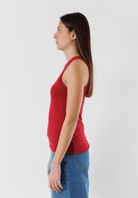 Top senza maniche di colore rosso realizzato in un tessuto liscio, design aderente, con scollatura rotonda e una leggera elasticità, indossato con jeans a vita alta.