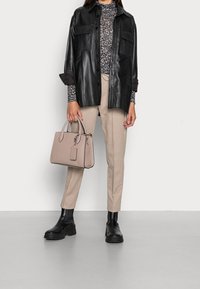 Svart läder oversized skjorta, mönstrad topp, beige byxor och svarta ankelstövlar. Håller en beige strukturerad handväska med detaljer.