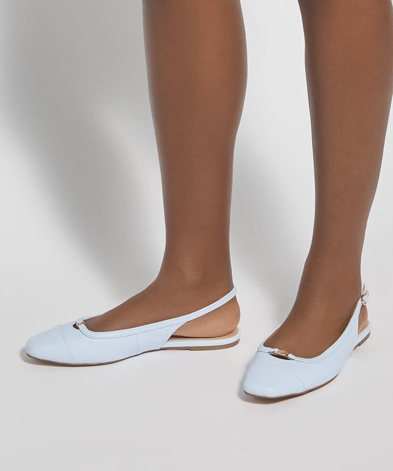 Jambes portant des ballerines slingback bleu clair à talons bas avec des ornements dorés sur un fond uni.