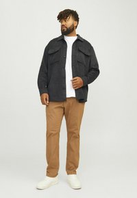 Dark gray button-up shirt with two chest pockets, worn over a white t-shirt. Tan chinos and white sneakers complete the outfit.