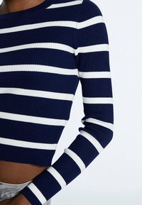 Top corto a righe blu navy e bianche in maglia a coste con maniche lunghe e scollo rotondo, che mostra un design aderente e un tessuto testurizzato.