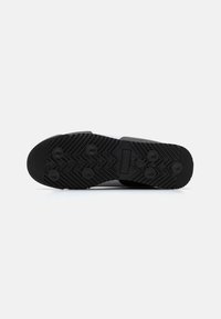 Semelle de chaussure en caoutchouc noir avec grip texturé et accents circulaires, présentant un motif en zigzag pour la traction et un profil plat.